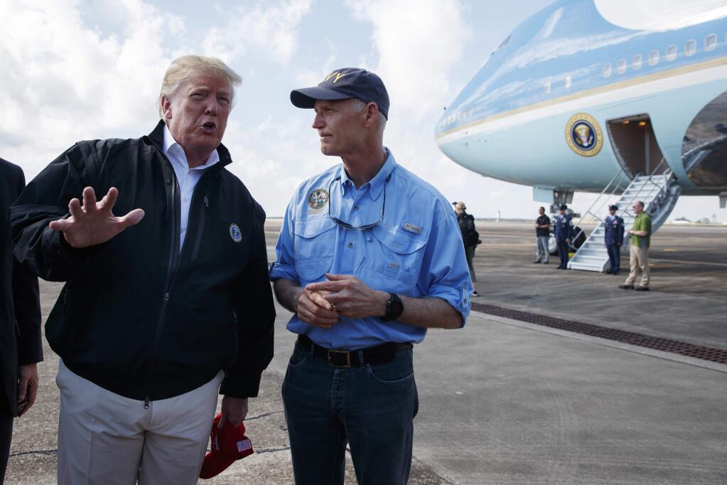 Gov. Rick Scott, R-Fla., right, looks on as President Donald Trump talks with reporters after arriving at Eglin Air Force Base to visit areas affected by Hurricane Michael, Monday, Oct. 15, 2018, in Eglin Air Force Base, Fla. (AP Photo/Evan Vucci)