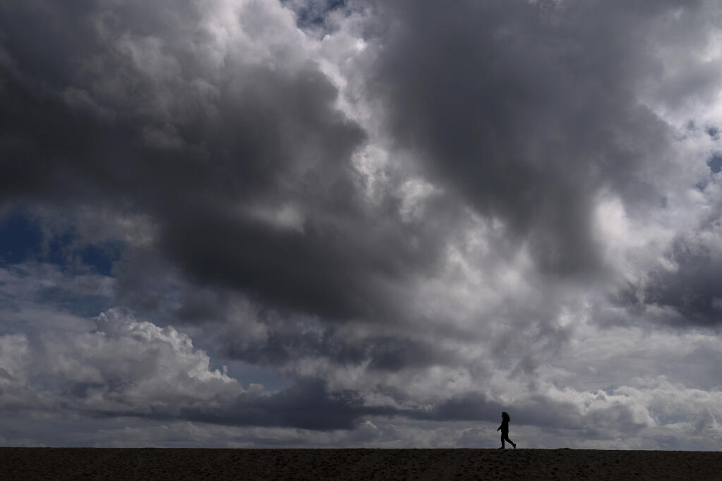 FILE - In this March 10, 2021, file photo, a woman strolls along the beach under rain clouds in Seal Beach, Calif. Rainstorms grew more erratic and droughts much longer across most of the U.S. West over the past half-century as climate change warmed the planet, according to a sweeping government study released, Tuesday, April 6, 2021, that concludes the situation in the region is worsening. (AP Photo/Jae C. Hong, File)