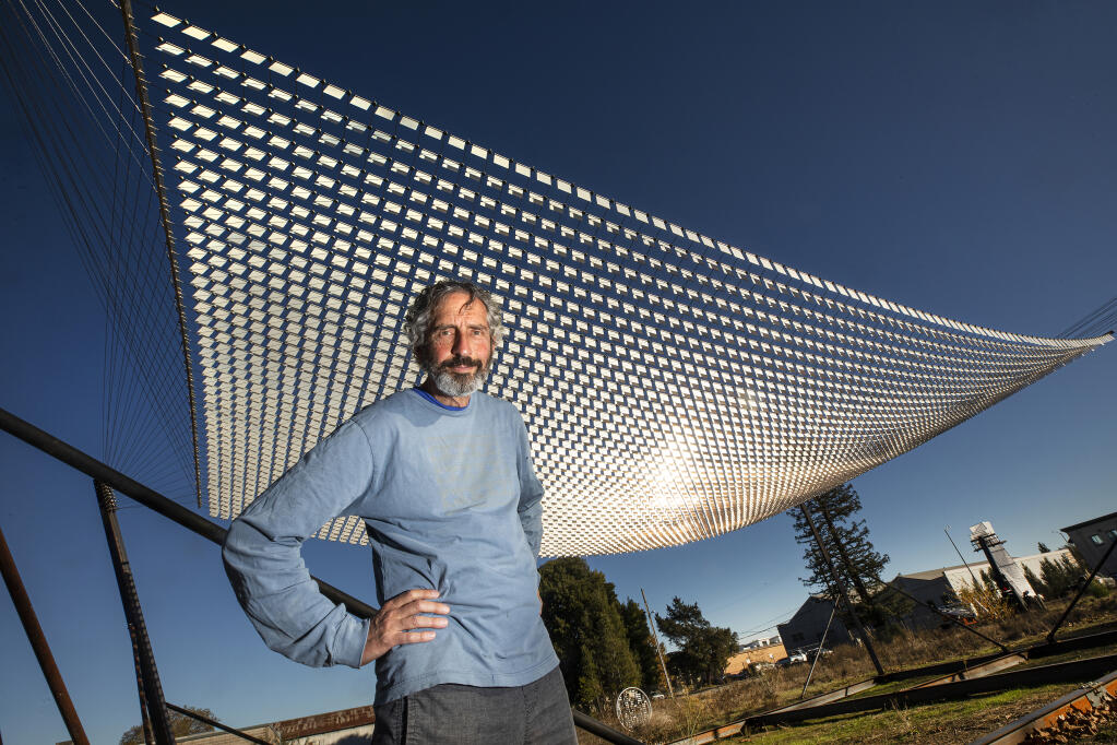 World-renowned artist Ned Kahn stands below his "Wind Hammock" with thousands of pivoting metal squares that move with the wind in a temporary "Air Garden" on the site of the future Hotel Sebastopol on Friday, Dec. 11, 2020. (John Burgess / The Press Democrat)