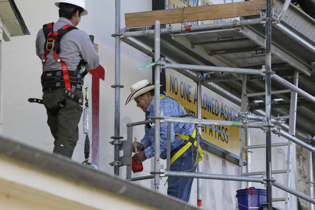 Dennis Turner, who took part in the Native American occupation, begins to repaint and restore messages painted above the main dock on Alcatraz Island Wednesday, Nov. 20, 2019, in San Francisco. About 150 people gathered at Alcatraz to mark the 50th anniversary of a takeover of the island by Native American activists. Original occupiers, friends, family and others assembled Wednesday morning for a program that included prayer, songs and speakers. They then headed to the dock to begin restoring messages painted by occupiers on a former barracks building. (AP Photo/Eric Risberg)