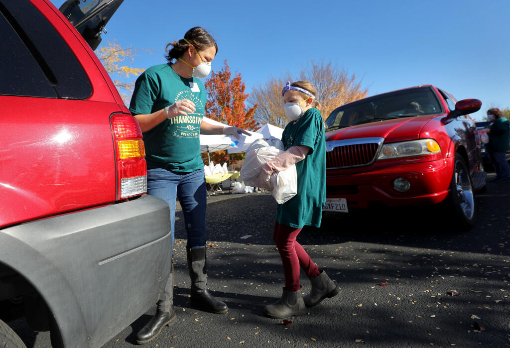 Kayla Patane, and her daughter, Addison, 8, load a recipient's vehicle with food for Thanksgiving during the Redwood Gospel Mission's The Great Thanksgiving Drive-Thru Event at Spring Hills Church in Santa Rosa on Wednesday, Nov. 25, 2020.  (Christopher Chung / The Press Democrat)