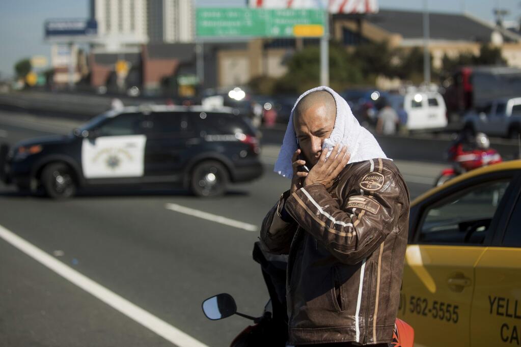 Stranded motorcyclist David Carr waits for Interstate 80 to reopen as police investigate the scene of a standoff with a suspect driving a sports utility vehicle on Wednesday, Sept. 27, 2017, in Emeryville, Calif. The incident, which ended in gunfire, shut freeway traffic in both directions at the height of morning rush hour. (AP Photo/Noah Berger)