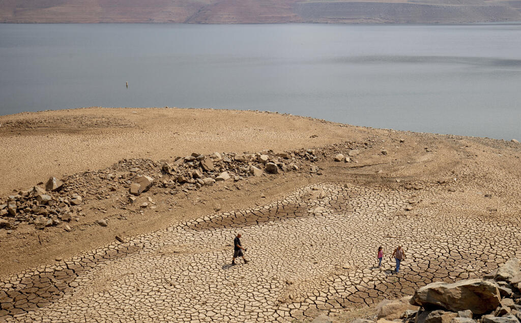 FILE - A family walks over cracked mud near Lake Oroville's shore as water levels remain low due to continuing drought conditions Sunday, Aug. 22, 2021, in Oroville, Calif. Cities and farms that rely on state water supplies will get 5% of what they requested in the new year, state water officials announced Thursday, Dec. 1, 2022. (AP Photo/Ethan Swope, File)