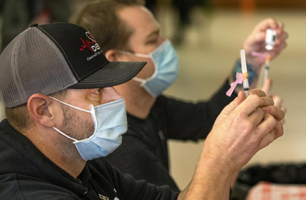 Paramedic Brandon Bruce, left, and RN Tim Adams fill syringes with doses of the Moderna COVID-19 vaccine for Phase 1 health care and care facility workers at the Roseland Regional Library vaccination site on Thursday, Jan. 22, 2021. (John Burgess / The Press Democrat)