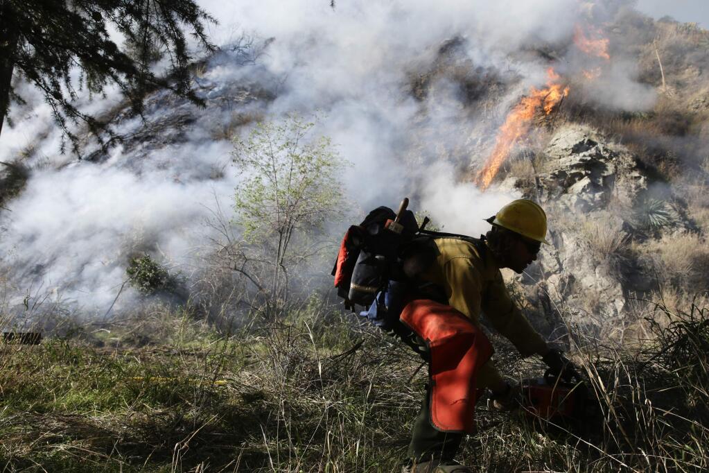 FILE - In this Jan. 17, 2014 file photo, a firefighter clears brush as firefighters continues to battle the Colby Fire near Azusa, Calif. California is calling in the National Guard for the first time to help protect communities from wildfires like the one that destroyed much of the city of Paradise last fall. The state is pulling the troops away from President Donald Trump's border protection efforts and devoting them to fire protection, another area where the president has been critical of California officials. (AP Photo/Jae C. Hong, File)