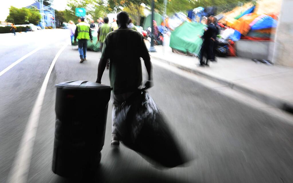 A homeless man helps to clean the Sixth Street underpass encampment. (KENT PORTER / The Press Democrat)