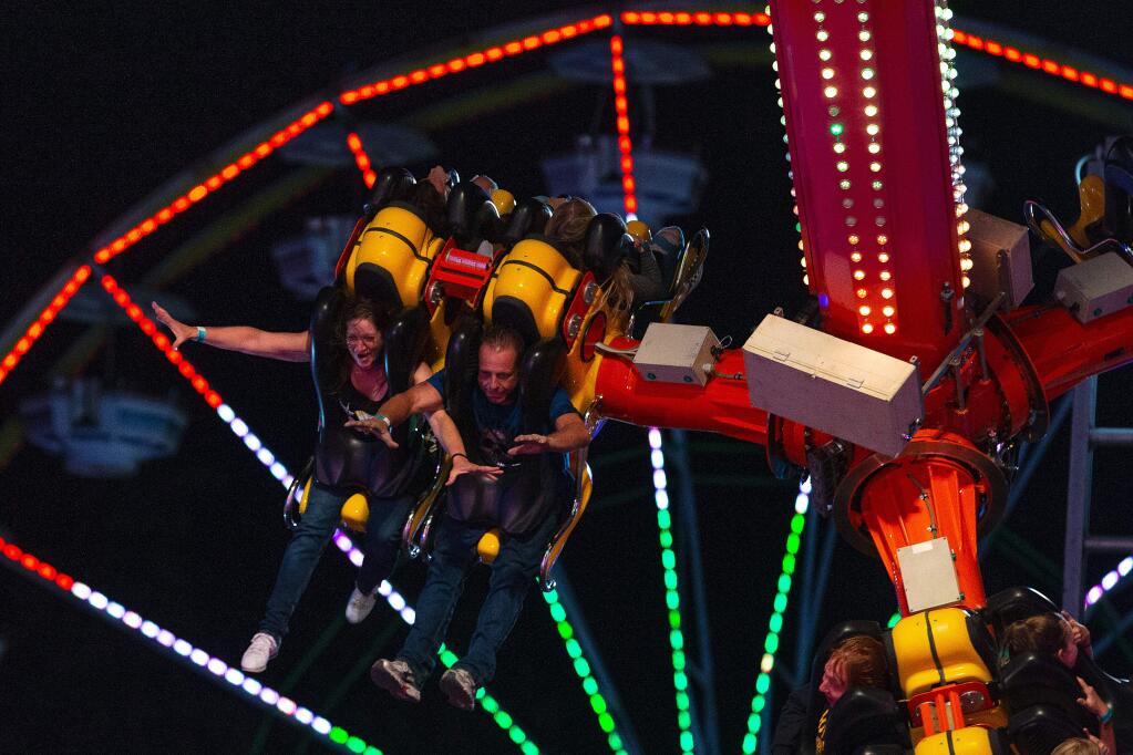 Heidi Montgomery, left, and Mike Medeiros, both of Santa Rosa raise their hands as they swoop down on the Inversion ride at the Sonoma County Fair, in Santa Rosa, California, on Thursday, August 1, 2019. (Alvin Jornada / The Press Democrat)