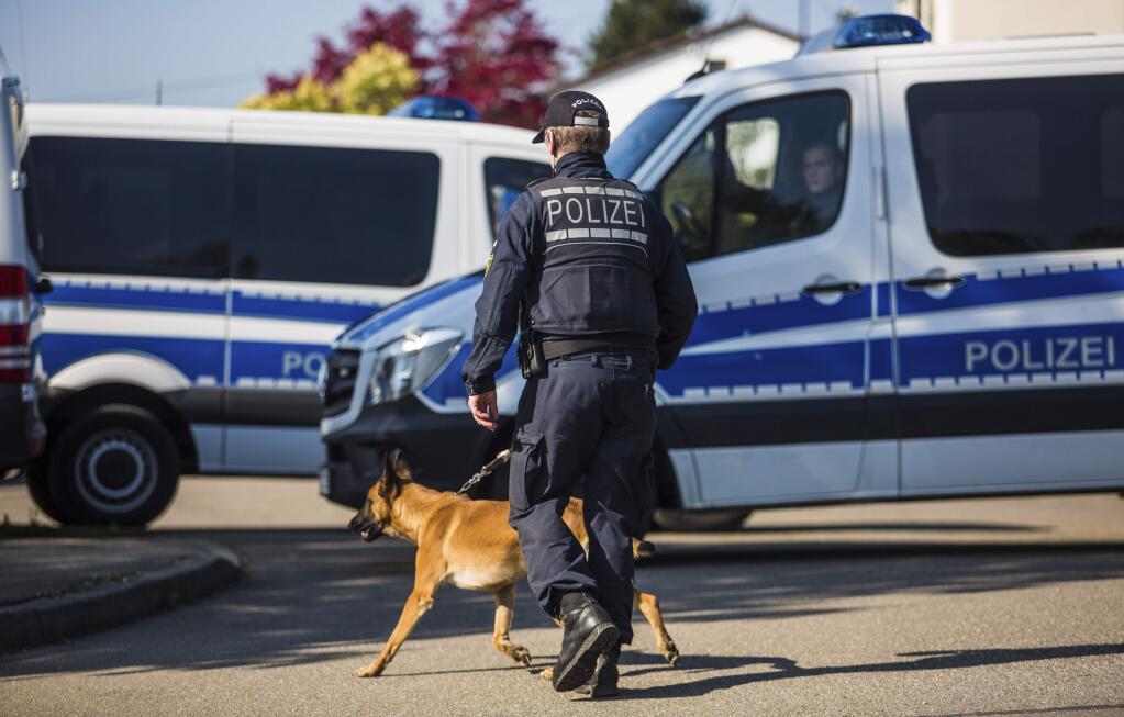 A police officer walks walks with a dog past police vehicles in a street in Rottenburg am Neckar, southern Germany, Friday, April 21, 2017 where a suspect was arrested in connection to the explosives attack on the team bus of Borussia Dortmund the week before. (Christoph Schmidt/dpa via AP)