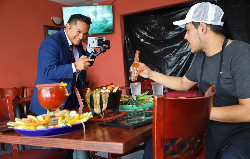 Neil Pacheco, left, films a Facebook live video for his 'What's Cookin' Sonoma County' page interviewing La Hoya Fine Mexican Cuisine co-owner Bryan Armendariz, featuring a few special dishes, in Rohnert Park on Monday, April 1, 2019. (Christopher Chung/ The Press Democrat)