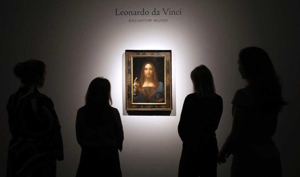 FILE- In this Oct. 24, 2017, file photo, people gather around Leonardo da Vinci's 'Salvator Mundi' on display at Christie's auction rooms in London. The rare painting of Christ, which that sold for a record $450 million, is heading to a museum in Abu Dhabi. The newly-opened Louvre Abu Dhabi made the announcement in a tweet on Wednesday, Dec. 6. (AP Photo/Kirsty Wigglesworth, File)