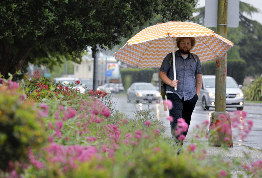Jack Lupin uses a beach umbrella to stay dry as he walks down Santa Rosa Avenue in Santa Rosa on Wednesday, May 15, 2019. (Beth Schlanker / The Press Democrat)