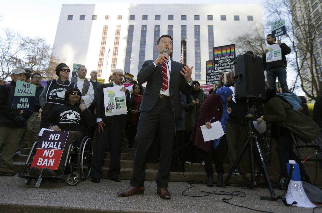 Washington Solicitor General Noah Purcell, center, speaks during a protest rally, Wednesday, Dec. 6, 2017, outside a federal courthouse in Seattle. The U.S. Supreme Court decision allowing President Donald Trump's third travel ban to take effect has intensified the attention on a legal showdown Wednesday before three judges in Seattle who have been cool to the policy as they hear arguments in Hawaii's challenge to the ban, which restricts travel to the United States by residents of six mostly Muslim countries and has been reviled by critics as discriminatory. (AP Photo/Ted S. Warren)