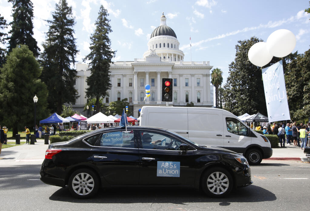 FILE - In this Aug. 28, 2019, file photo, dozens of supporters of a measure to limit when companies can label workers as independent contractors circle the Capitol during a rally in Sacramento, Calif. On Monday, Aug. 10, 2020, a California judge ordered ride-hailing companies Uber and Lyft to treat their drivers as employees, not contractors. It's the first ruling in what is expected to be a drawn-out legal battle over implementation of a new state law relating to the gig economy. The companies will likely appeal the ruling, which would delay its implementation. (AP Photo/Rich Pedroncelli, File)