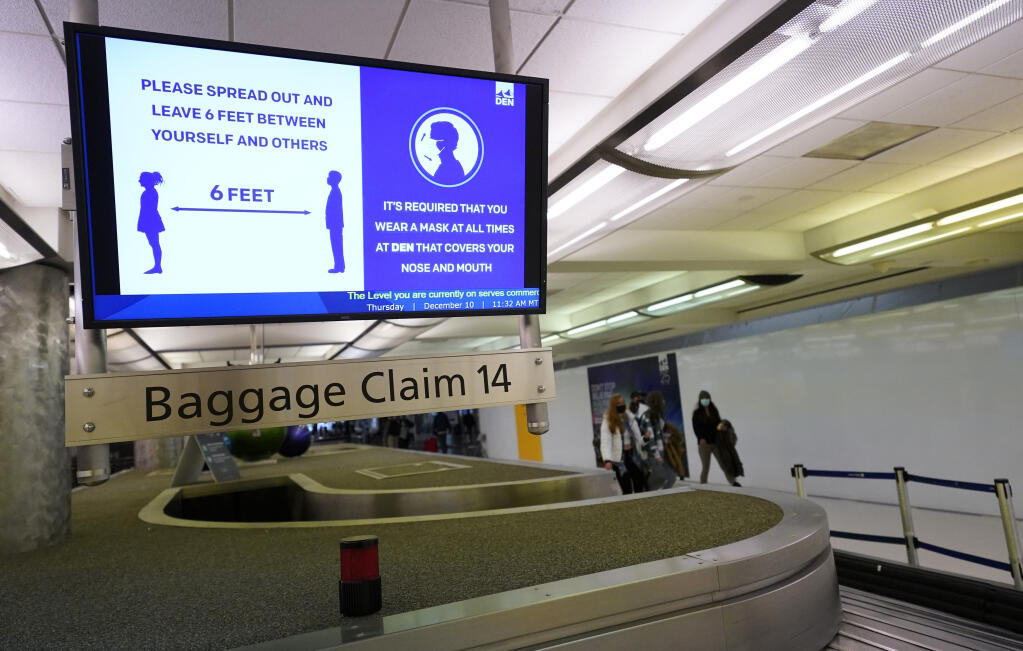 FILE - In this Dec. 10, 2020, file photo, an electronic sign warns travelers to maintain social distance in the terminal of Denver International Airport in Denver. Federal officials said Monday, May 10, 2021 they are pursuing civil penalties against two more passengers for interfering with airline crews, the latest in a surge of such cases in recent months. (AP Photo/David Zalubowski, File)