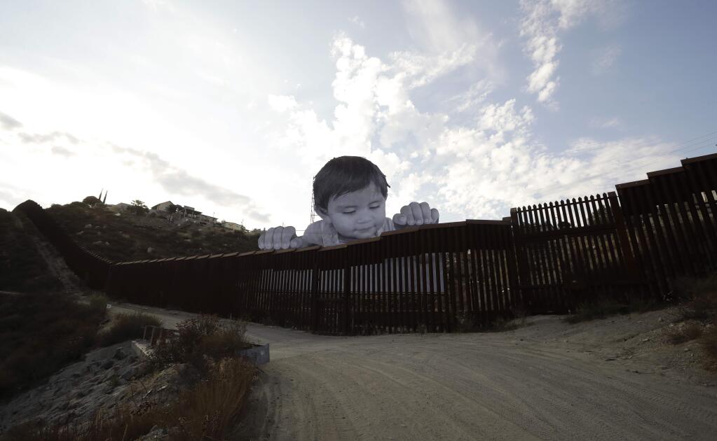 HOLD FOR STORY A mural in Tecate, Mexico, sits just beyond a border structure Friday, Sept. 8, 2017, seen from Tecate, Calif. A French artist aiming to prompt discussions about immigration erected a 65-foot-tall cut-out photo of a Mexican boy, pasting it to scaffolding built in Mexico. The image overlooks a section of wall on the California border and will be there for a month. (AP Photo/Gregory Bull)