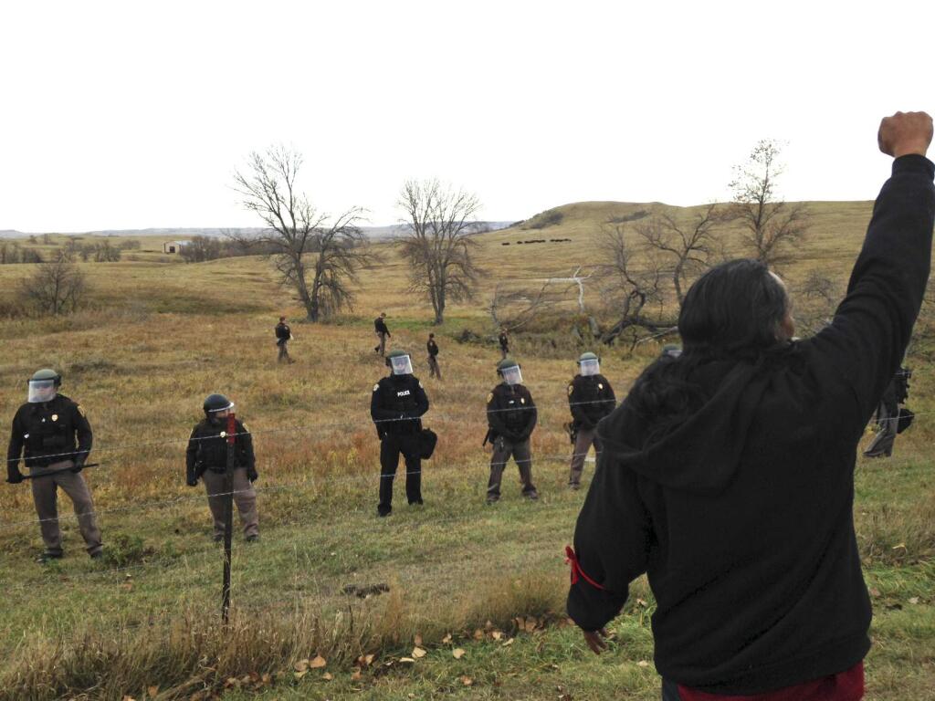 A Dakota Access pipeline protester defies law enforcement officers who are trying to force them from a camp on private land in the path of pipeline construction, Thursday, Oct. 27, 2016 near Cannon Ball, N.D. Soldiers and law enforcement officers dressed in riot gear began arresting protesters who had set up a camp on private land to block construction of the Dakota Access oil pipeline. (AP Photo/James MacPherson)