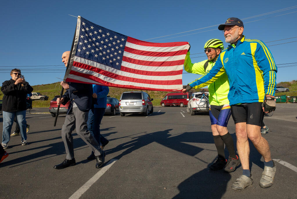 Sebastopol veterans riding in the Old Glory Relay, from right, Bill Sauber, 74, and Bob Rogers, 81, help carry the American flag with Roy Cratty, 90, on his short walk to end the 123-mile day from Westport to Lucas Wharf in Bodega Bay, April 11, 2023. The relay, which will end in Atlanta, is raising money for to help veterans become more physically active. (John Burgess/The Press Democrat)