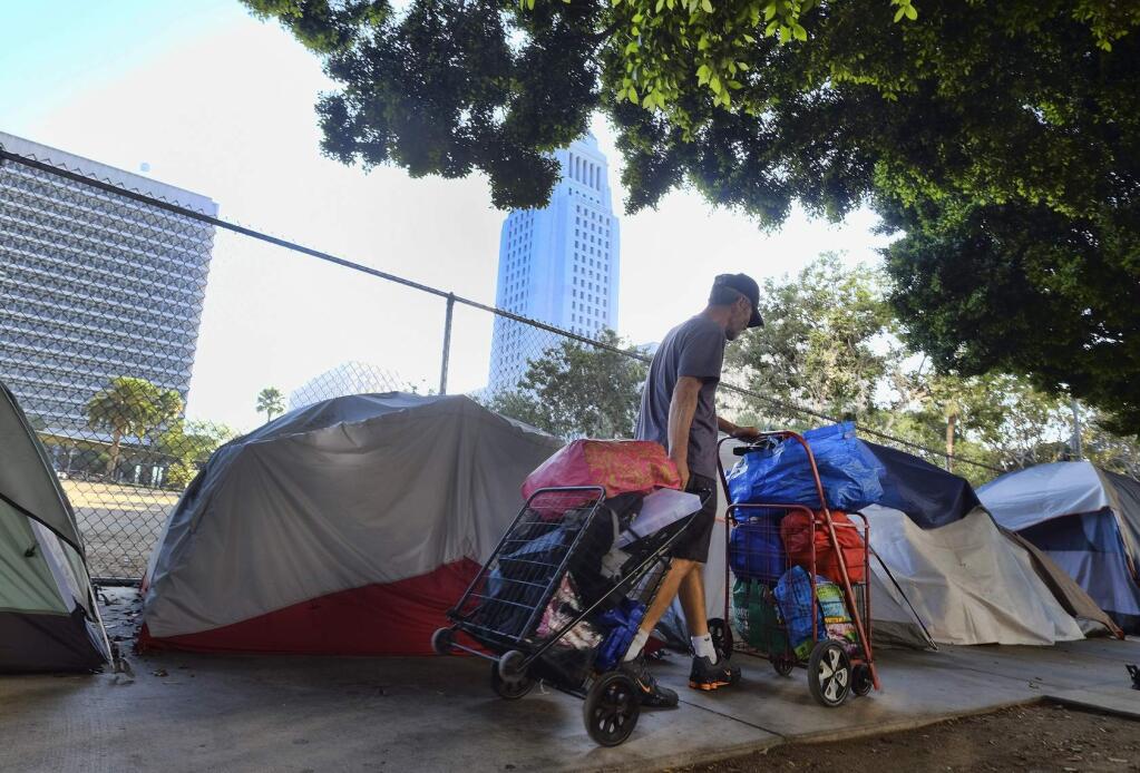 FILE - In this Monday, July 1, 2019 file photo, a homeless man moves his belongings from a street behind Los Angeles City Hall as crews prepared to clean the area. (AP Photo/Richard Vogel,File)