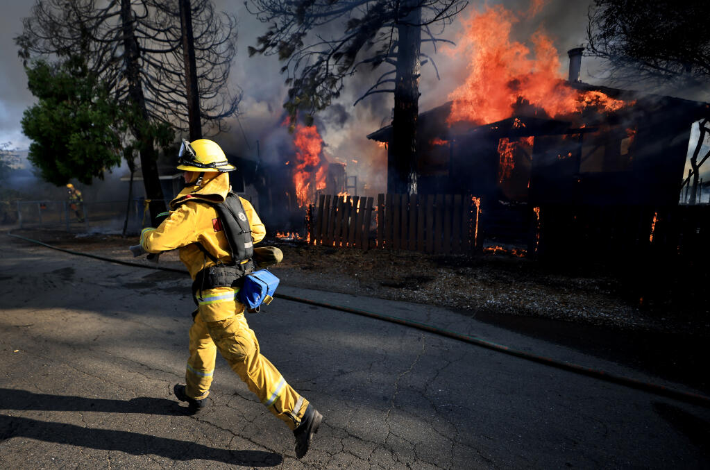 Un bombero del Distrito de Protección contra Incendios de Northshore corre para ayudar a descargar la manguera contra incendios de las unidades de bomberos que llegan durante un incendio que quemó cinco casas en Clearlake Oaks, el domingo 18 de julio de 2021 (Kent Porter / The Press Democrat) 2021.