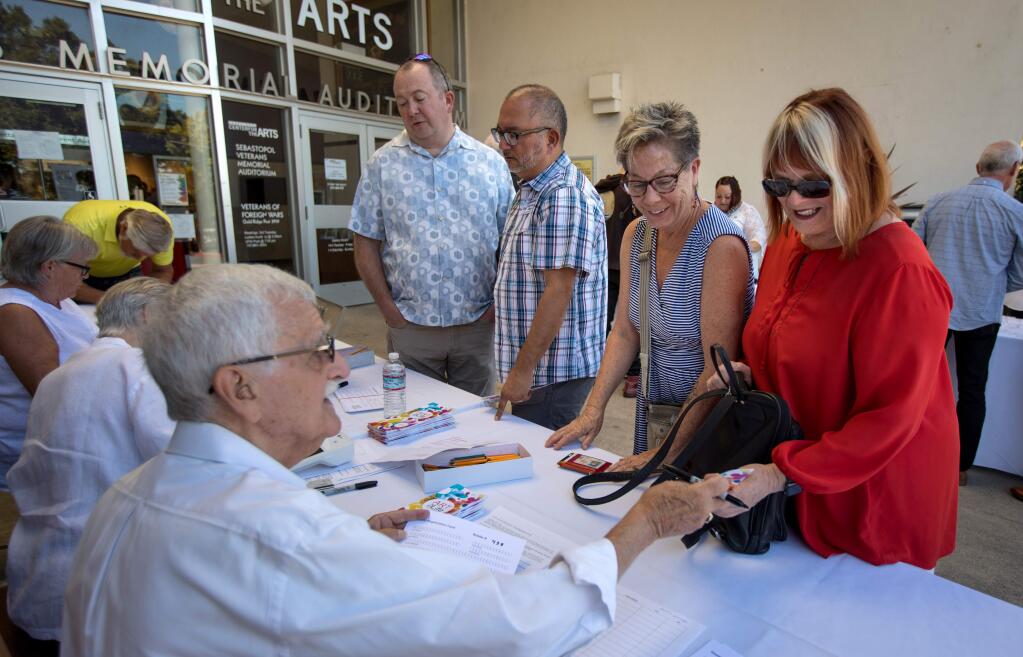 Volunteer Mike O'Malley, seated left, checks in Teresa Weinberger and Lorraine Blue, right, both of Santa Rosa, at the 'Art for Life' benefit held at Sebastopol Center for the Arts on Saturday, Sept. 21, 2019. (DARRYL BUSH/ FOR THE PD)