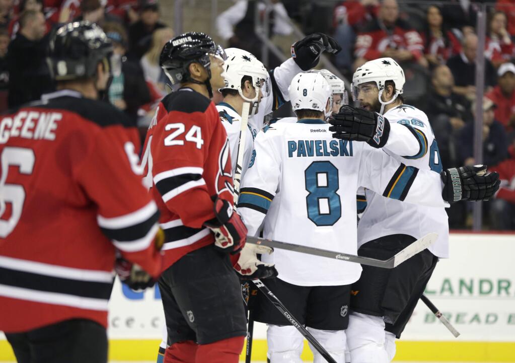 San Jose Sharks players, in white, congratulate center Joe Pavelski (8) after he scored a goal against the New Jersey Devils during the first period of an NHL hockey game, Saturday, Oct. 18, 2014, in Newark, N.J. (AP Photo/Julio Cortez)