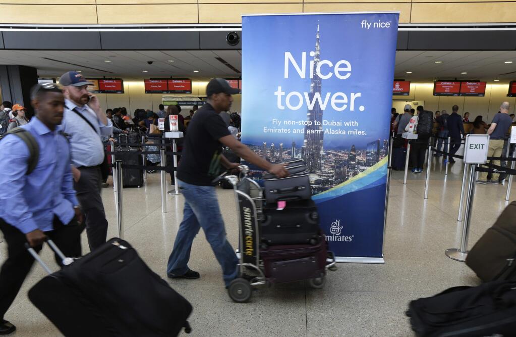 Travelers walk past a sign advertising Emirates flights from Seattle to Dubai at the Seattle-Tacoma International Airport, Monday, June 26, 2017, in Seattle. The U.S. Supreme Court said Monday that President Donald Trump's travel ban on visitors from Iran, Libya, Somalia, Sudan, Syria and Yemen can be enforced if those visitors lack a 'credible claim of a bona fide relationship with a person or entity in the United States,' and that justices will hear full arguments in October 2017 (AP Photo/Ted S. Warren)