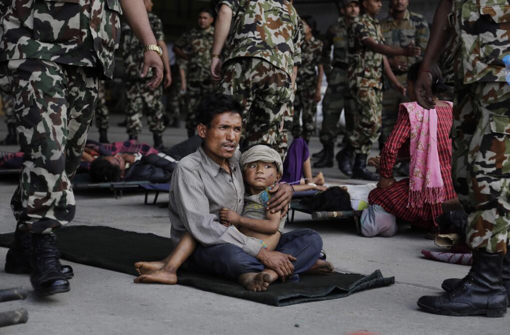 A man sits with a child on his lap as victims of Saturdayís earthquake, wait for ambulances after being evacuated at the airport in Kathmandu, Nepal, Monday, April 27, 2015. The death toll from Nepal's earthquake is expected to rise depended largely on the condition of vulnerable mountain villages that rescue workers were still struggling to reach two days after the disaster. (AP Photo/Altaf Qadri)