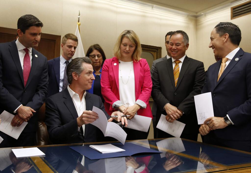 California Gov. Gavin Newsom, seated, talks with Assemblyman Phil Ting, D-San Francisco, second from right, before signing Ting's measure that allows employers, co-workers and teachers to seek gun violence restraining orders for people they believe to be a danger to themselves or others, during a signing ceremony at the Capitol in Sacramento, Calif., Friday, Oct. 11, 2019. Ting's bill was one of more than a dozen gun control bills the governor signed Friday. (AP Photo/Rich Pedroncelli)