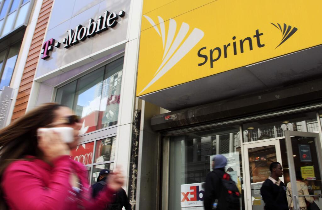 FILE- In this April 27, 2010 file photo, a woman using a cell phone walks past T-Mobile and Sprint stores in New York. T-Mobile and Sprint are trying again to combine in a deal that would reshape the U.S. wireless landscape, the companies announced Sunday, April 29, 2018 (AP Photo/Mark Lennihan, File)
