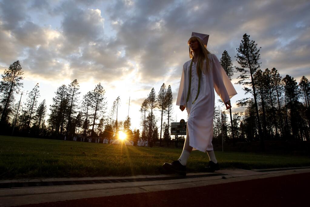 In white cap and gown a graduating senior walks to the graduation ceremonies at Paradise High School in Paradise, Calif., Thursday June 6, 2019. Most of the students of Paradise High lost their homes when the Camp Fire swept through the area and the school was forced to hold classes in Chico. The seniors gathered one more time at Paradise High for graduation ceremonies. (AP Photo/Rich Pedroncelli)