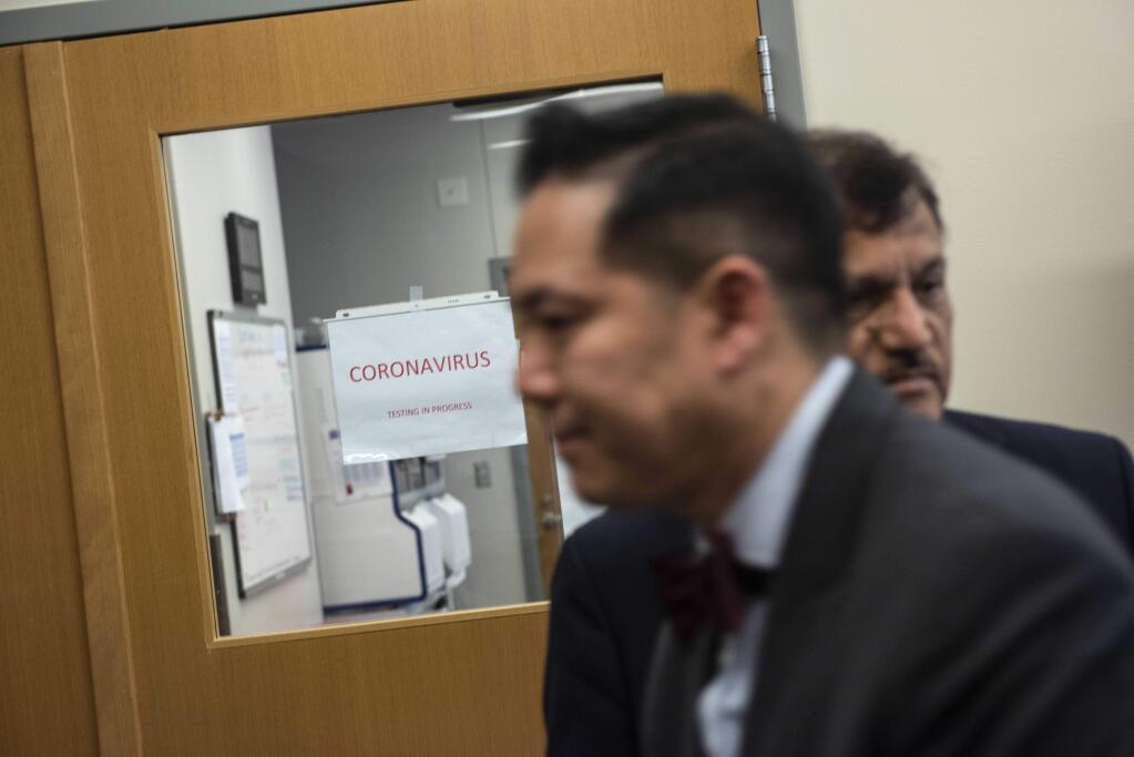 Anthony Tran, center, the public health laboratory director for the D.C. Department of Forensic Sciences, walks in front of a lab dedicated to coronavirus testing in Washington on March 30. (Washington Post photo by Michael Robinson Chavez)