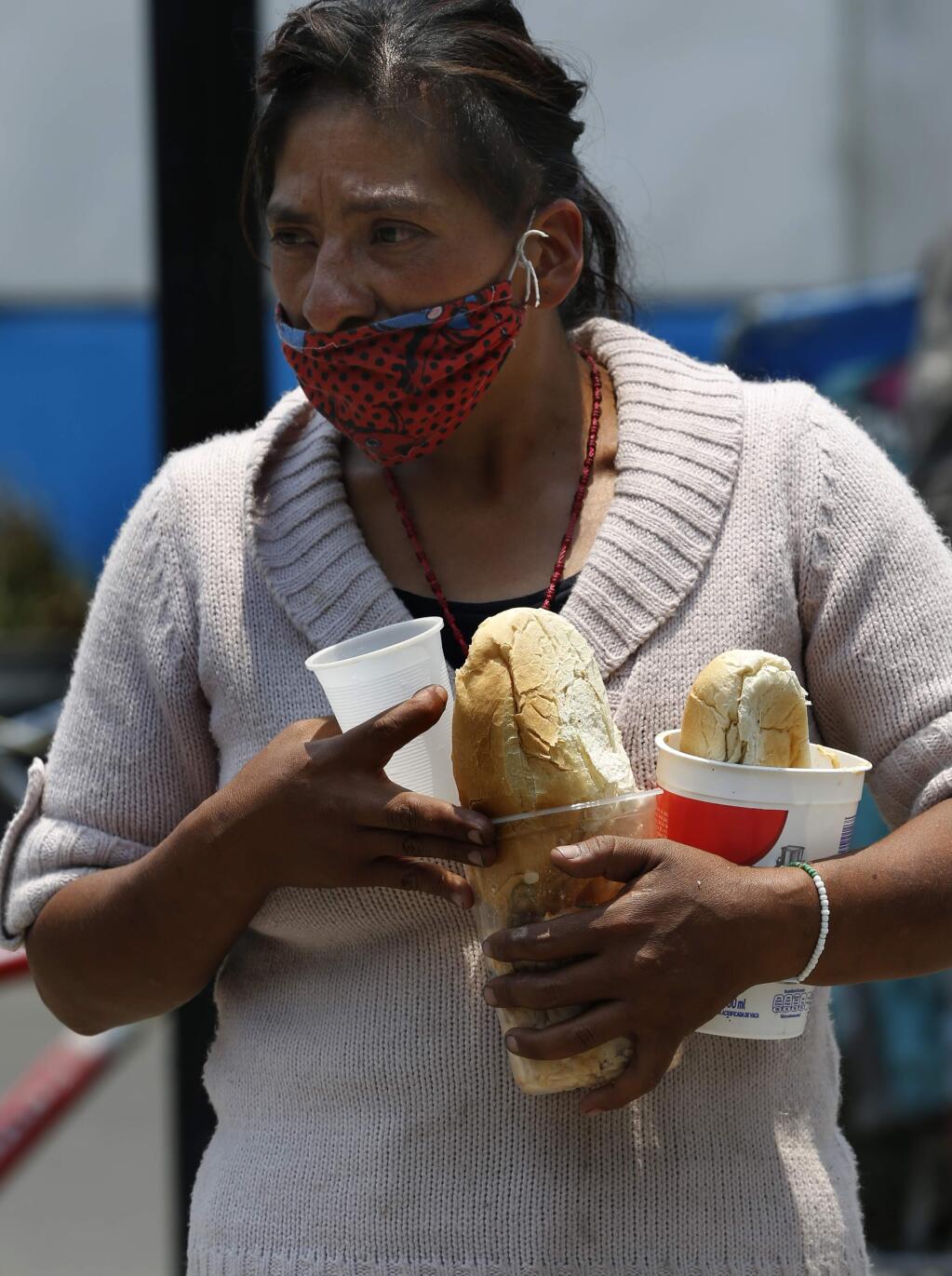 A woman wearing a mask against the spread of the new coronavirus carries a meal that she got from the mobile dining rooms program as people who have not been able to work because of the COVID-19 pandemic line up for a meal outside the Iztapalapa hospital in Mexico City, Wednesday, May 20, 2020. (AP Photo/Marco Ugarte)