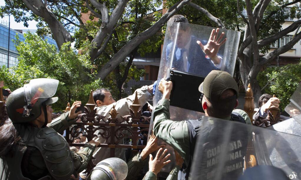 National Assembly President Juan Guaido, Venezuela's opposition leader, tries to climb the fence past National Guards to enter the compound of the Assembly, after he and other opposition lawmakers were blocked by police from entering a session to elect new Assembly leadership in Caracas, Venezuela, Sunday, Jan. 5, 2020. With Guaido stuck outside, a rival slate headed by lawmaker Luis Parra swore themselves in as leaders of the single-chamber legislature. (AP Photo/Andrea Hernandez Briceño)