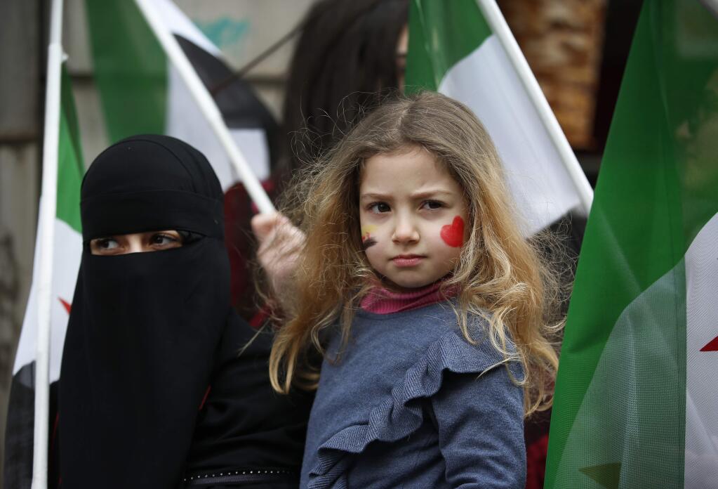 A woman holds a child amidst Syrian flags as she joins others protesting attacks on rebel-held suburb of eastern Ghouta in Syria's capital Damascus, during a rally outside the Russian Consulate in Istanbul, Thursday, Feb. 22, 2018. Scores of people have gathered chanting Syrian songs and slogans denouncing a Syrian government forces' bombing campaign that has targeted hospitals, apartment blocks and other civilian sites. Hundreds of people have been killed or wounded in the campaign in recent days. (AP Photo/Lefteris Pitarakis)