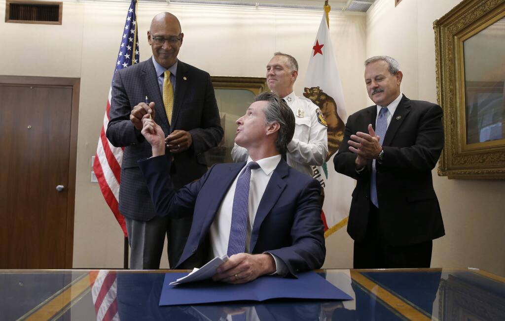 Gov. Gavin Newsom hands Assemblyman Chris Holden, D-Pasadena, left, the pen he used to sign Holden's wildfire bill as Thom Porter, the director for the California Department of Forestry and Fire Protection, center, and Mark Ghilarducci, the director of the California Governor's Office Emergency Services, right, look on in Sacramento, Calif., Friday, July 12, 2019. The bill AB1054, is aimed at stabilizing the state's electric utilities in the face of devastating wildfires caused by their equipment. (AP Photo/Rich Pedroncelli)