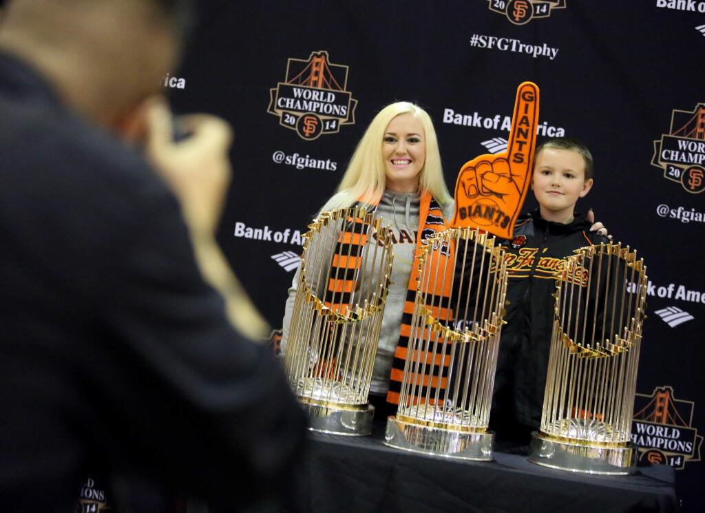 Acacia McAlpin, center, and Cyrus Balzer, 8, of Guerneville have their photo taken with the San Francisco Giants World Series trophies at the Finley Community Center in Santa Rosa, Saturday, January 10, 2015. (Crista Jeremiason / The Press Democrat)