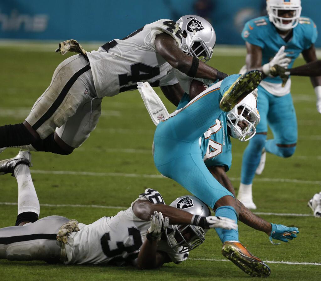 Miami Dolphins wide receiver Jarvis Landry is up ended by Oakland Raiders cornerback T.J. Carrie, bottom, and strong safety Karl Joseph during the first half Sunday, Nov. 5, 2017, in Miami Gardens, Fla. (AP Photo/Wilfredo Lee)