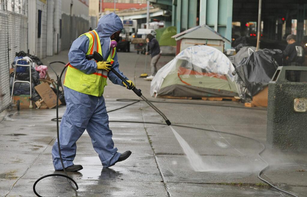 A city worker uses a power washer to clean the sidewalk by a tent city along Division Street in San Francisco in 2016. (ERIC RISBERG / Associated Press)