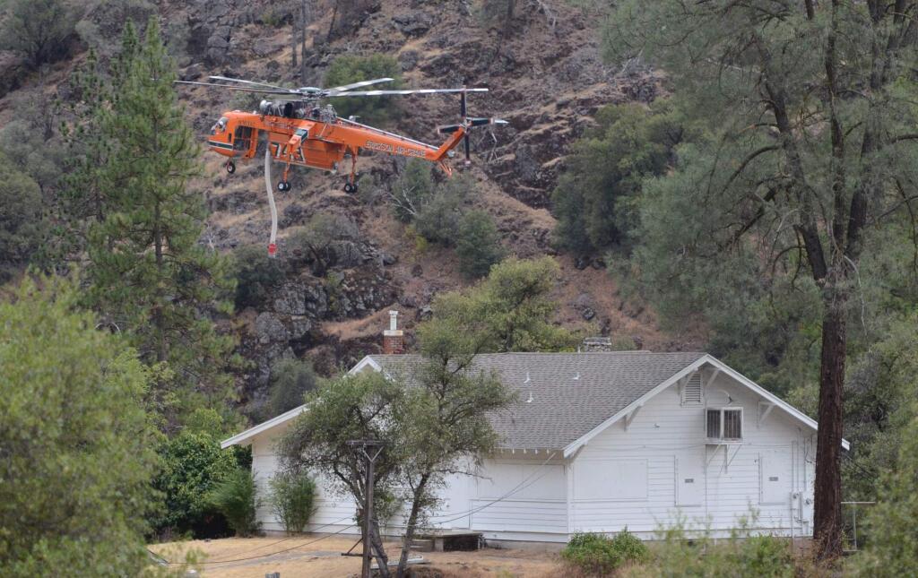A helicopter hovers above a home as it prepares to dip water from the nearby Merced River in El Portal, Calif., on Monday, July 28, 2014.(AP Photo/The Fresno Bee, Mark Crosse)