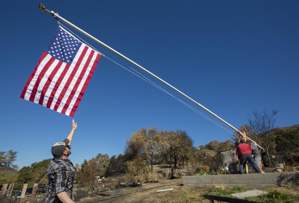 As the flag is raised, Dave Shultz ensures it doesn't touch the ground. Ramona Nicholson, of the Nicholson Ranch, lost everything to the recent fires - her home and car, her father's house, farm machinery, an olive orchard, a barn and stables, and two train boxcars that were a familiar site to anyone who drove past her vineyards on Napa Rd. Last week, she decided to raise a flag on a 40-foot flagpole that was installed many years ago by her late father, Socrates Nicholson. With a little help from her friends, the flag - a symbol of survival and hope - now flies from the top of a hill on the ranch, overlooking the Carneros vineyards. (Photo by Robbi Pengelly/Index-Tribune)