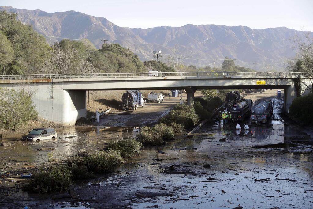 FILE - In this Jan. 13, 2018 file photo, crews work to clear U.S. Highway 101 in the aftermath of a mudslide in Montecito, Calif.A California utility facing a slew of lawsuits over a deadly wildfire in Southern California is now suing Santa Barbara County and the state's transportation department, saying they neglected to prepare for deadly mudslides that followed the blaze. Southern California Edison filed a lawsuit Friday, Jan. 18, 2019 against the county and the California Department of Transportation (Caltrans) over mudslides last year that killed 23 people and destroyed hundreds of homes in Montecito. (AP Photo/Marcio Jose Sanchez, File)