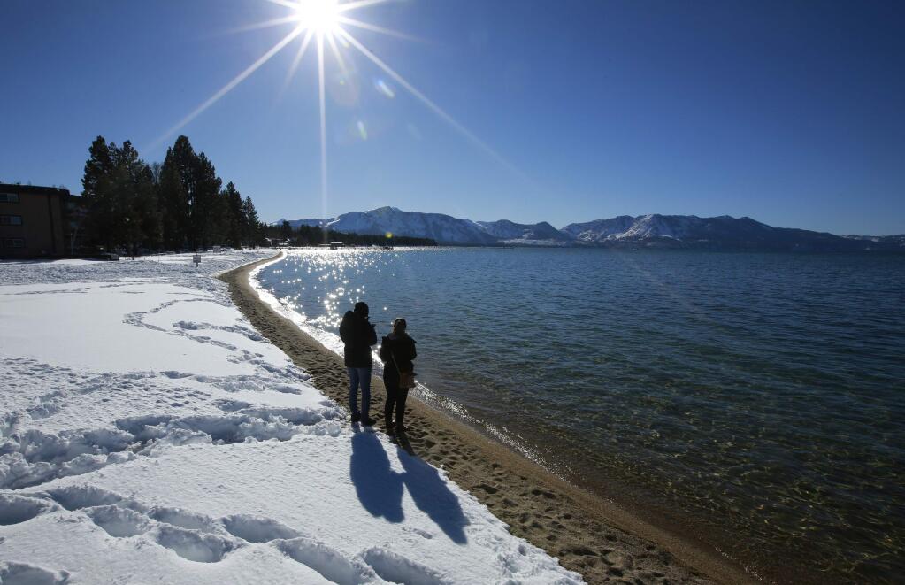 FILE - In this March 5, 2018 file photo, sunlight shimmers off the snow and waters of Lake Tahoe in South Lake Tahoe, Calif. Water stored at Lake Tahoe has nearly reached its legal limit after snowmelt from a stormy winter left behind enough to potentially last through up to three summers of drought. The lake has been within an inch of its maximum allowed surface elevation of 6,229.1 feet above sea level for more than three weeks and crept to within a half-inch this week. (AP Photo/Rich Pedroncelli, File)