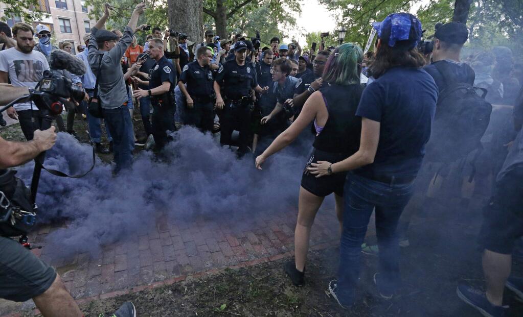 Police and protesters react to a smoke bomb as some protesters are removed during a rally to remove the confederate statue known as Silent Sam from campus at the University of North Carolina in Chapel Hill, N.C., Monday, Aug. 20, 2018. (AP Photo/Gerry Broome)