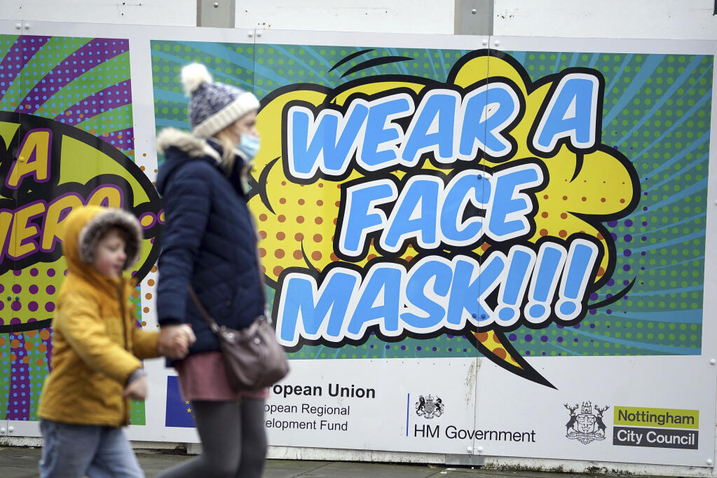 People walk past a billboard inviting citizens to wear face masks to curb the spread of COVID-19, in Nottingham, England, Monday Dec. 20, 2021. Britain’s health secretary has refused to rule out imposing tougher COVID-19 restrictions before Christmas amid the rapid rise of infections and continuing uncertainty about the omicron variant.  (Mike Egerton/PA via AP)