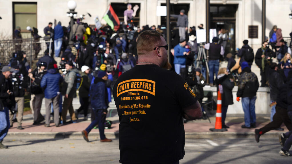 An unidentified man wearing an Oath Keepers shirt stands outside the Kenosha County Courthouse, Friday, Nov. 19, 2021 in Kenosha, Wis., the day Kyle Rittenhouse was acquitted of all charges in the deadly Kenosha shootings that became a flashpoint in the nation's debate over guns, vigilantism and racial injustice. (AP Photo/Paul Sancya)