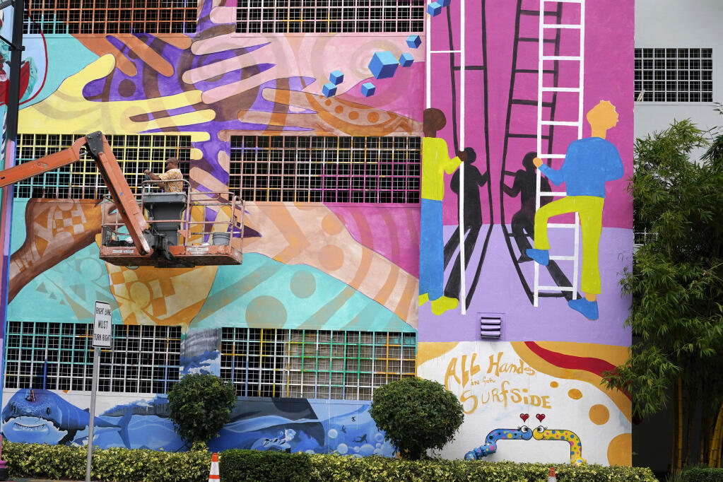 Mural artist Kyle Holbrook paints a mural, Wednesday, July 14, 2021, in Miami, in the memory of the victims of the Champlain Towers South building in Surfside, Fla. which partially collapsed nearly three weeks ago. (AP Photo/Lynne Sladky)