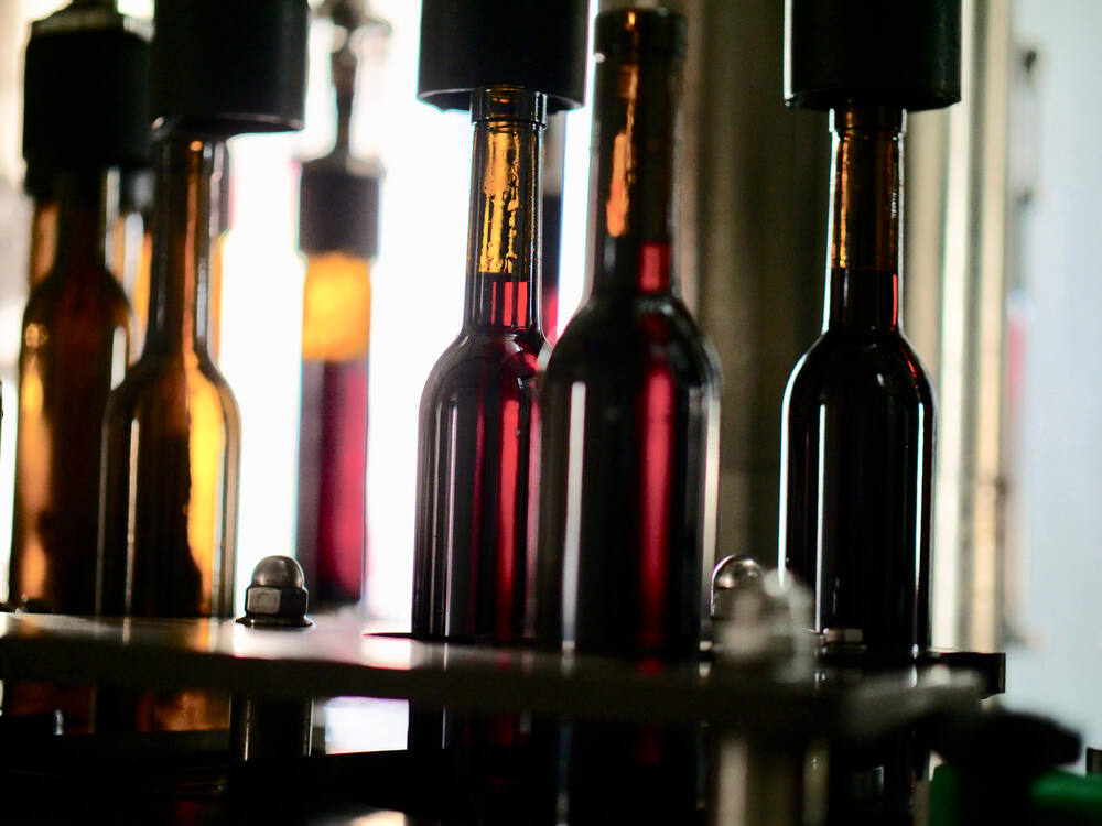 Amber-colored bottles are filled with red wine and sealed on a winery bottling line.