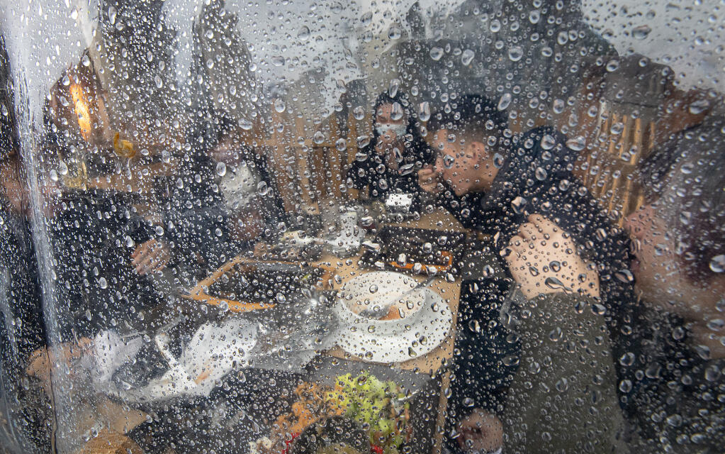 Friends have lunch inside the plastic tarped seating area at the new Mi Ranchito Downtown restaurant on 5th Street in Santa Rosa on a rainy Friday, Nov. 13, 2020. (John Burgess / The Press Democrat)