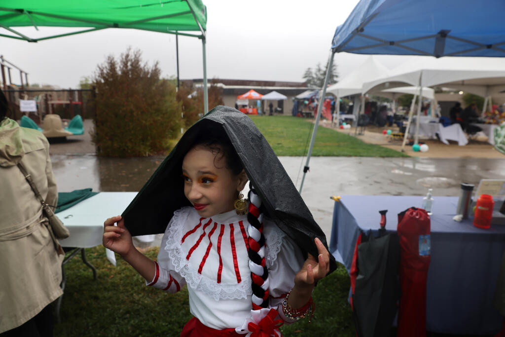 Yoselyn Ochoa 10, tries to stay dry under her costume bag after performing with the group Ireri Ballet Folklorico Petaluma during the Fiesta de Independencia at the Luther Burbank Center for the Arts in Santa Rosa, Calif. on Sunday, September 18, 2022. (Beth Schlanker/The Press Democrat)