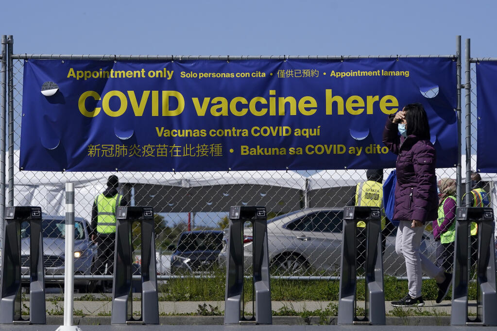 FILE - In this March 4, 2021, file photo, a pedestrian wears a face mask while walking past a sign at a vaccination center at City College of San Francisco during the coronavirus pandemic in San Francisco. Before California throws open its coronavirus vaccine program to all adults on April 15, there will be a two-week window when millions of people between the ages of 50 and 64 can get their shot. The rollout for this age group, who become eligible on Thursday, April 1, has prompted an uptick in appointment requests.  (AP Photo/Jeff Chiu, File)